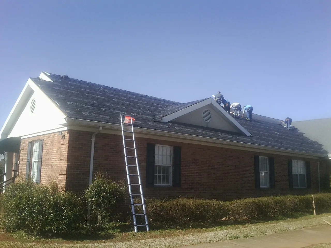 Crew tearing shingles off a brick ranch roof with a ladder set — Emergency Roof Repair work by our crew in Markham