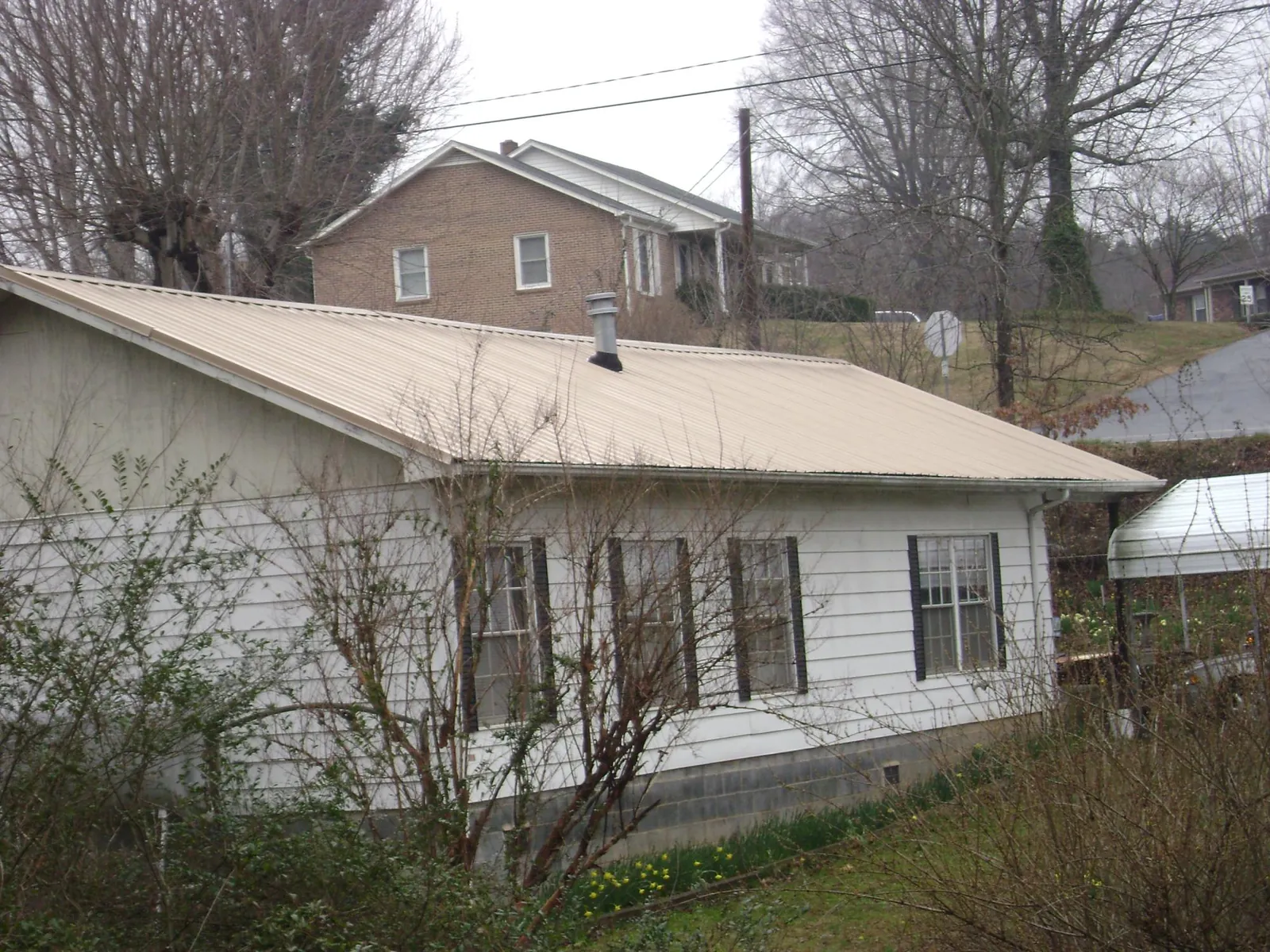 Tan metal roof on a white sided house set into a hillside — Commercial Roofing by Roofing Brothers in Markham